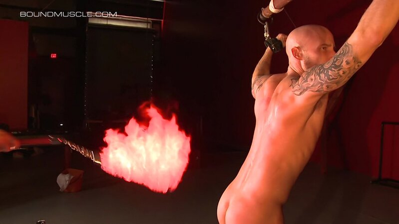 Luke Riley brings a flaming flogger dangerously close to the skin of Drake Jaden