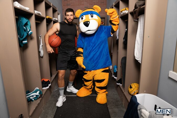 Mascot Jake Preston buries his tongue in athlete Shamu Azizam in the locker