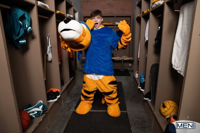 Mascot Jake Preston buries his tongue in athlete Shamu Azizam in the locker