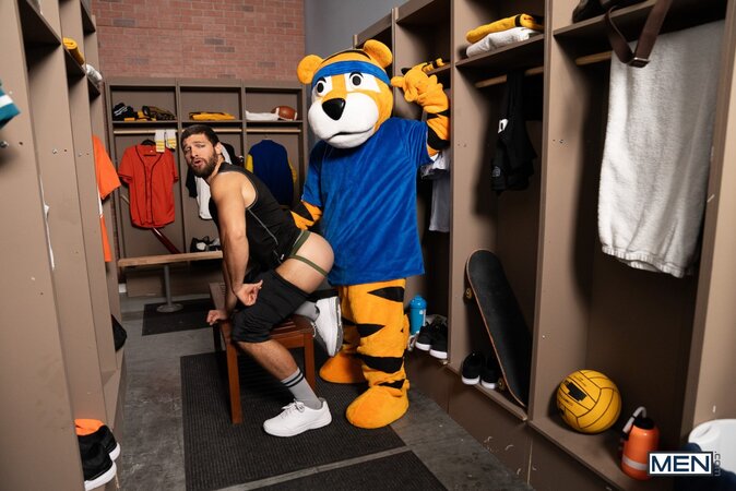 Mascot Jake Preston buries his tongue in athlete Shamu Azizam in the locker