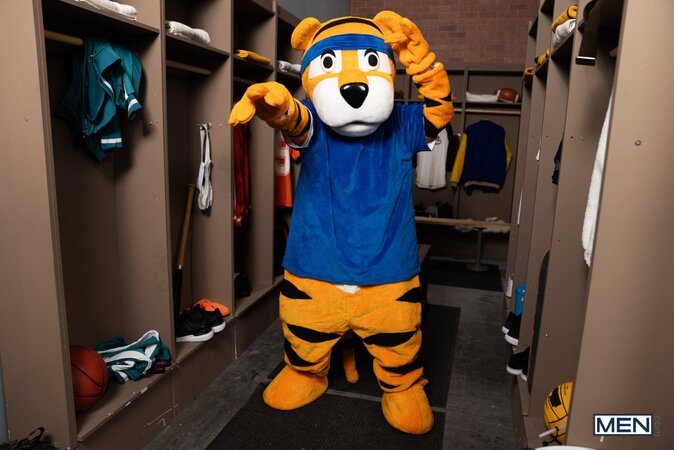Mascot Jake Preston buries his tongue in athlete Shamu Azizam in the locker