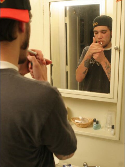 Zack smokes a cigarette while shaving in bathroom